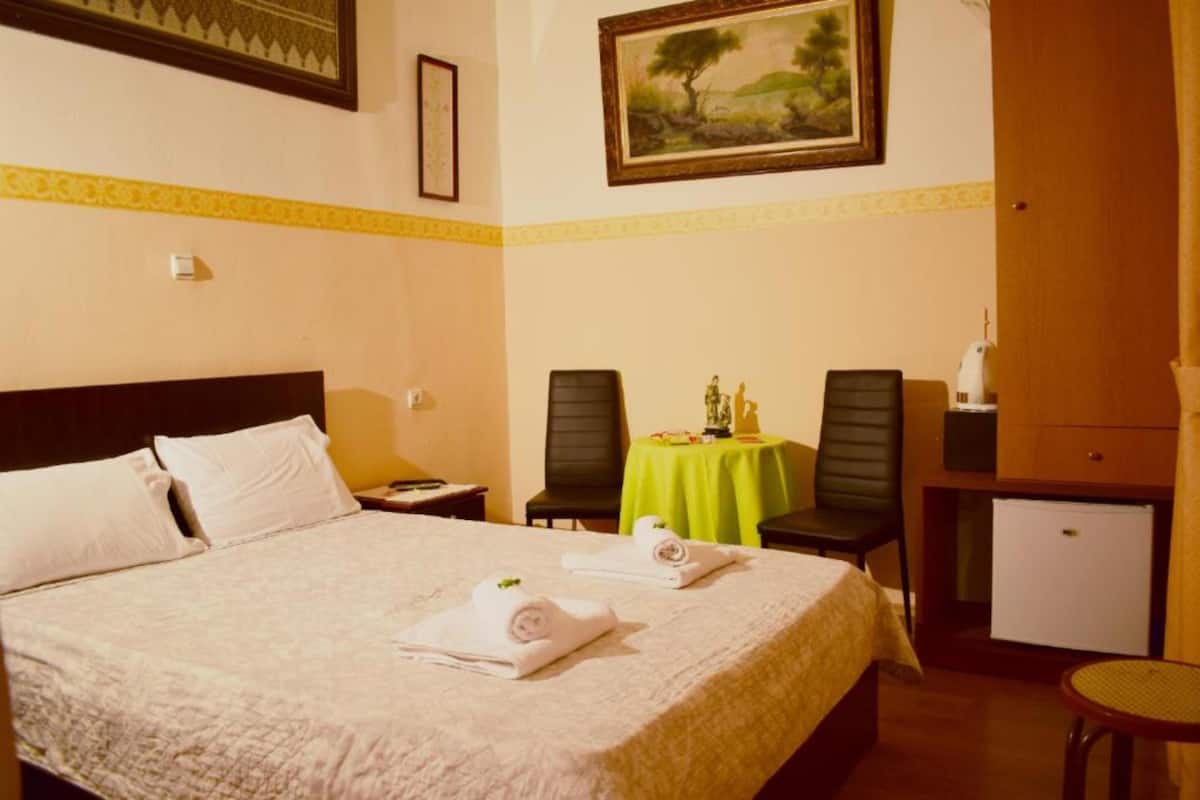 Une chambre d’hôtel comprenant un lit, deux chaises, une petite table recouverte d’une nappe verte, un bureau avec un ordinateur et un mini-réfrigérateur.
