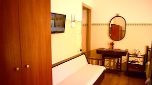 Quarto com um banco de madeira, uma mesinha com um vaso, um espelho e uma televisão na parede.
