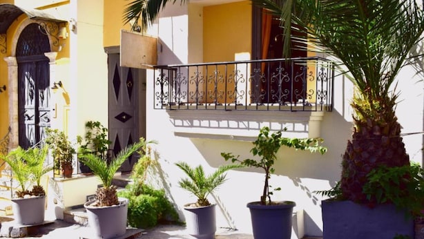 Um edifício com varanda, plantas em vasos e uma porta com detalhes em ferro.