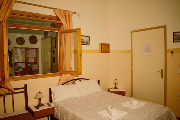 A hotel room with a bed, a nightstand, a lamp, a window with curtains, a door, and a mirror. - Stoa Rooms Chania Old Port (Chania)