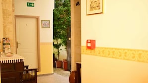 Um corredor estreito com uma porta marcada '4', uma pequena mesa com toalha branca e um extintor de incêndio vermelho na parede direita.