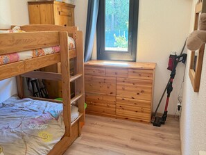 A bunk bed with a wooden dresser and a vacuum cleaner in a room with a window.