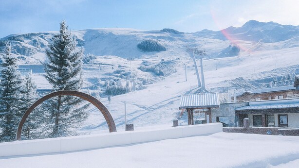 A snow-covered landscape with a ski lift, a wooden structure, and a large metal arch. - Comfortable studio for 4 with piste view, ski-in/ski-out access (Les Menuires)