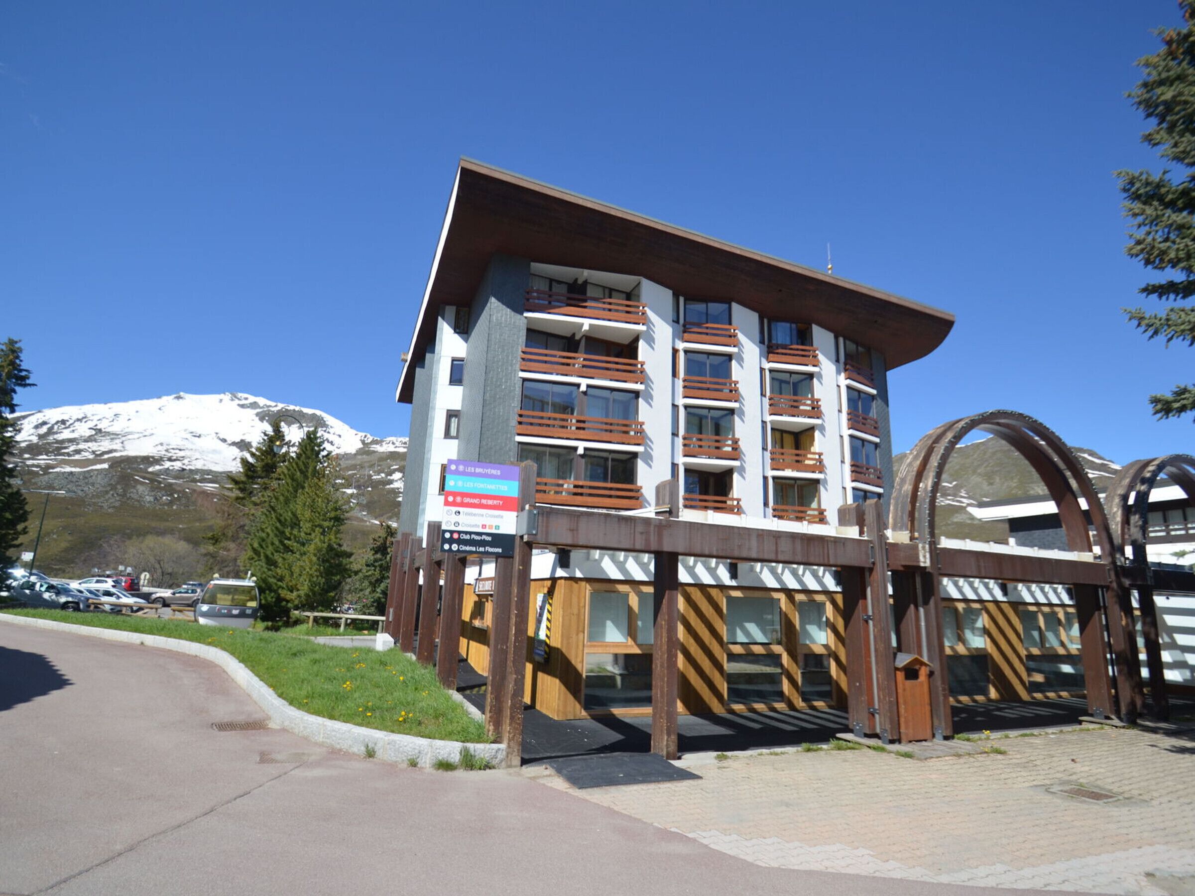 Un hotel de varios pisos con balcones, un complejo de esquí al fondo y un cielo despejado.