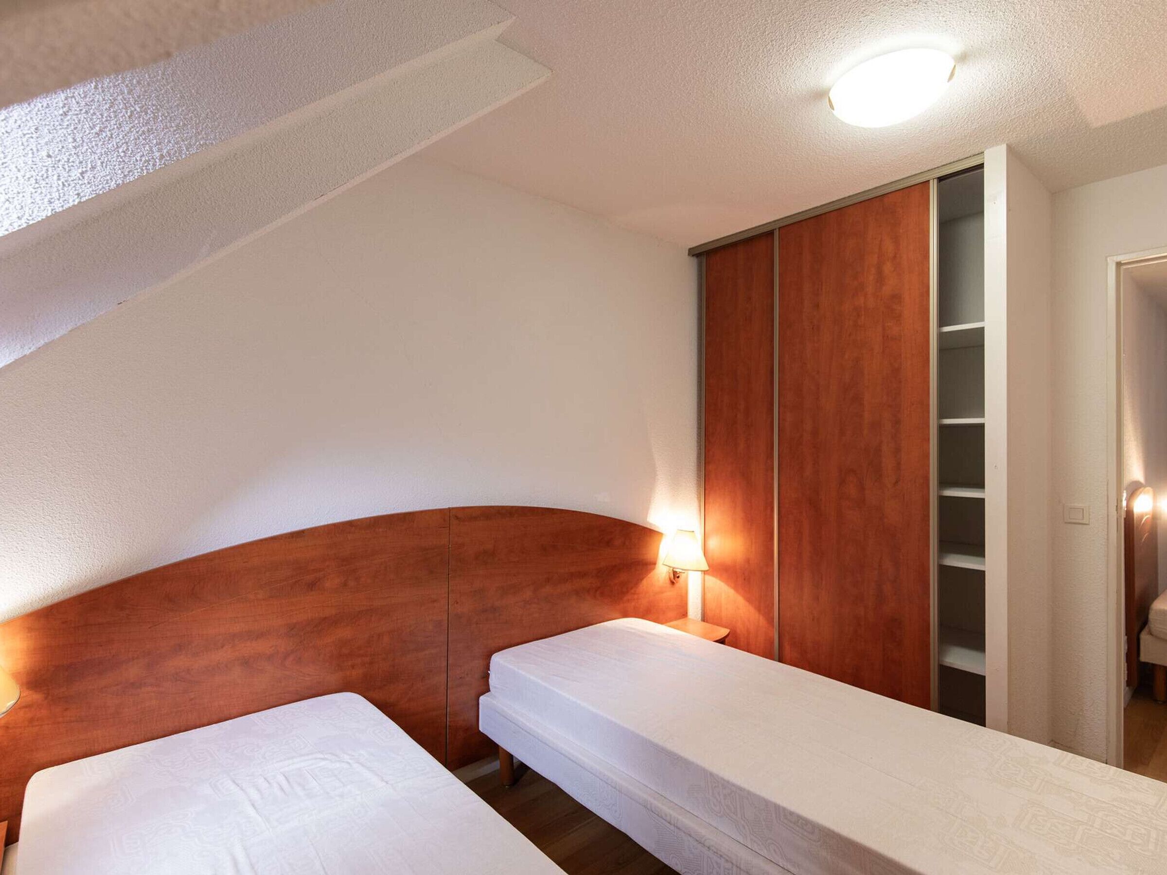 Un dormitorio con dos camas individuales, cabecero de madera, mesita de noche con lámpara y armario con espejo.