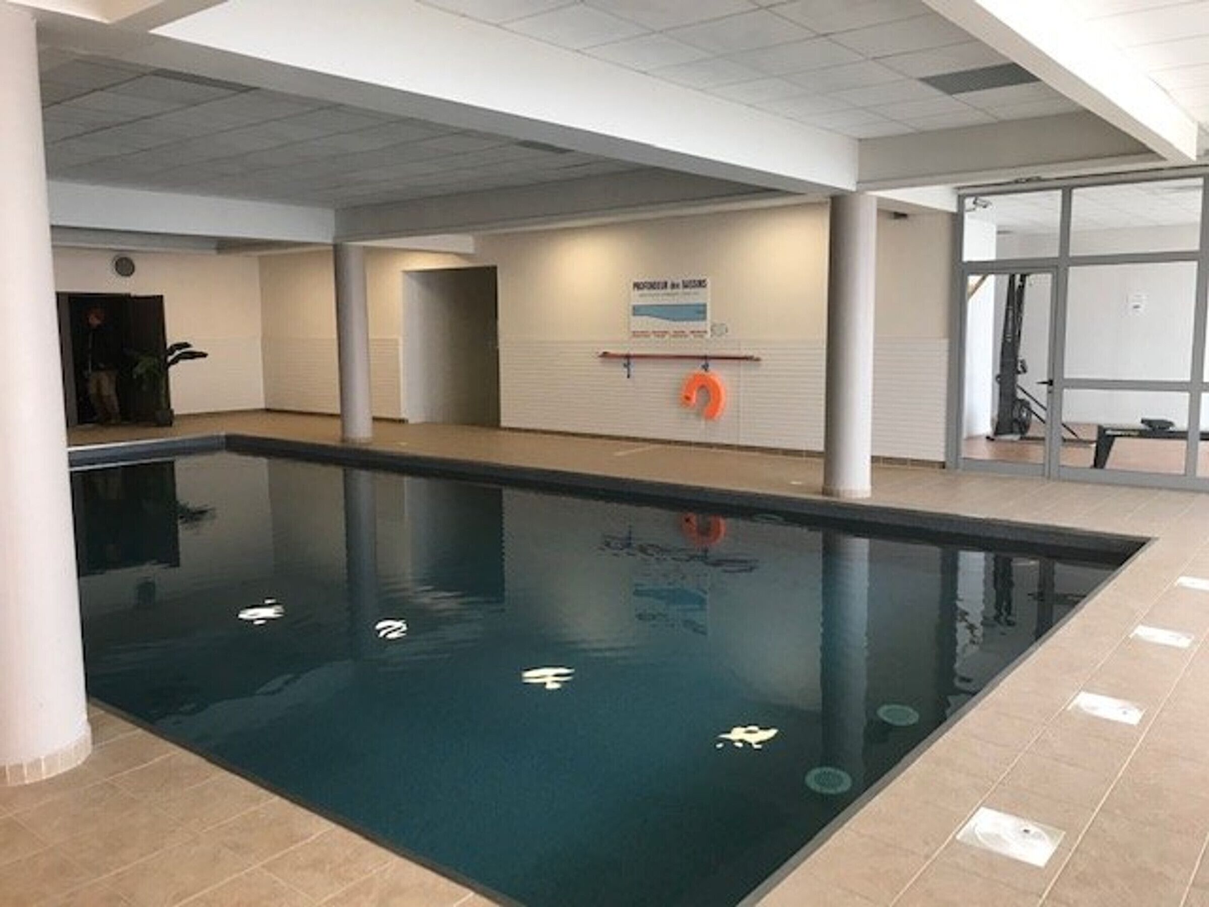 Een binnenzwembad met helder water, betegelde wanden en een reddingsboei aan de muur.
