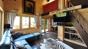 Interior de una cabaña con sofá, televisor, paredes de madera y alfombra de cebra.