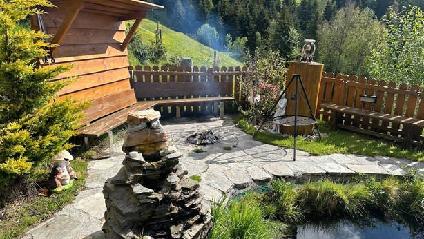 Una cabaña rústica de madera con un muro de piedra, una terraza de madera y un pequeño estanque.