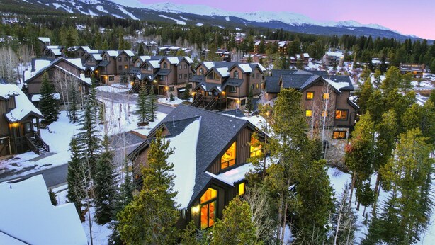 Ein Resort mit mehreren Chalet-ähnlichen Gebäuden, umgeben von schneebedeckten Bäumen und Bergen im Hintergrund.