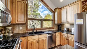 Eine Küche mit Holzausstattung, einem Edelstahlkühlschrank, einem eingebauten Backofen und einem Fenster mit Blick auf Bäume.
