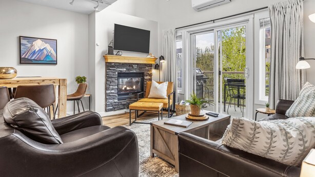 Una sala de estar moderna con sofás de cuero, una chimenea, un televisor de pantalla plana y ventanas amplias.