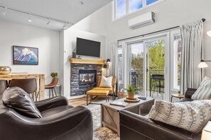 A modern living room with leather sofas, a fireplace, a flat-screen TV, and large windows. - Charming Mountain Loft | Pet Friendly | Mountain Views! (canmore)