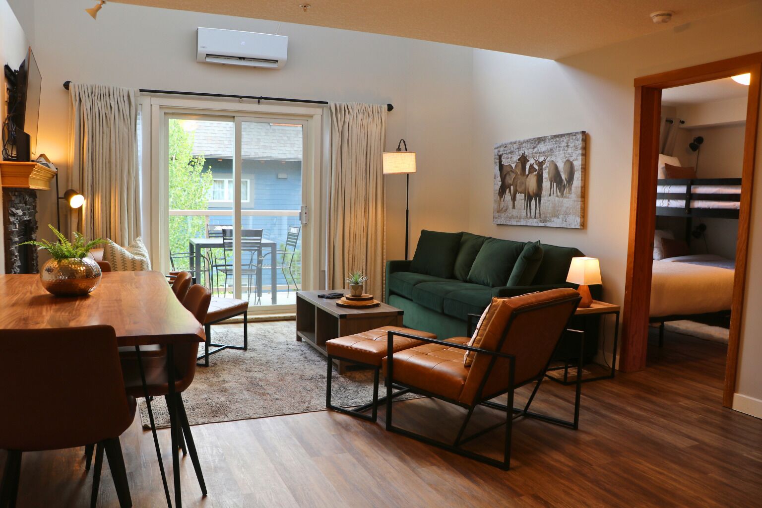 A cozy living room with a green sofa, brown leather chairs, a dining table with chairs, a coffee table, and a painting on the wall.