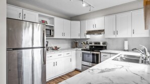 Una cocina moderna con armarios blancos, electrodomésticos de acero inoxidable y encimera de mármol.