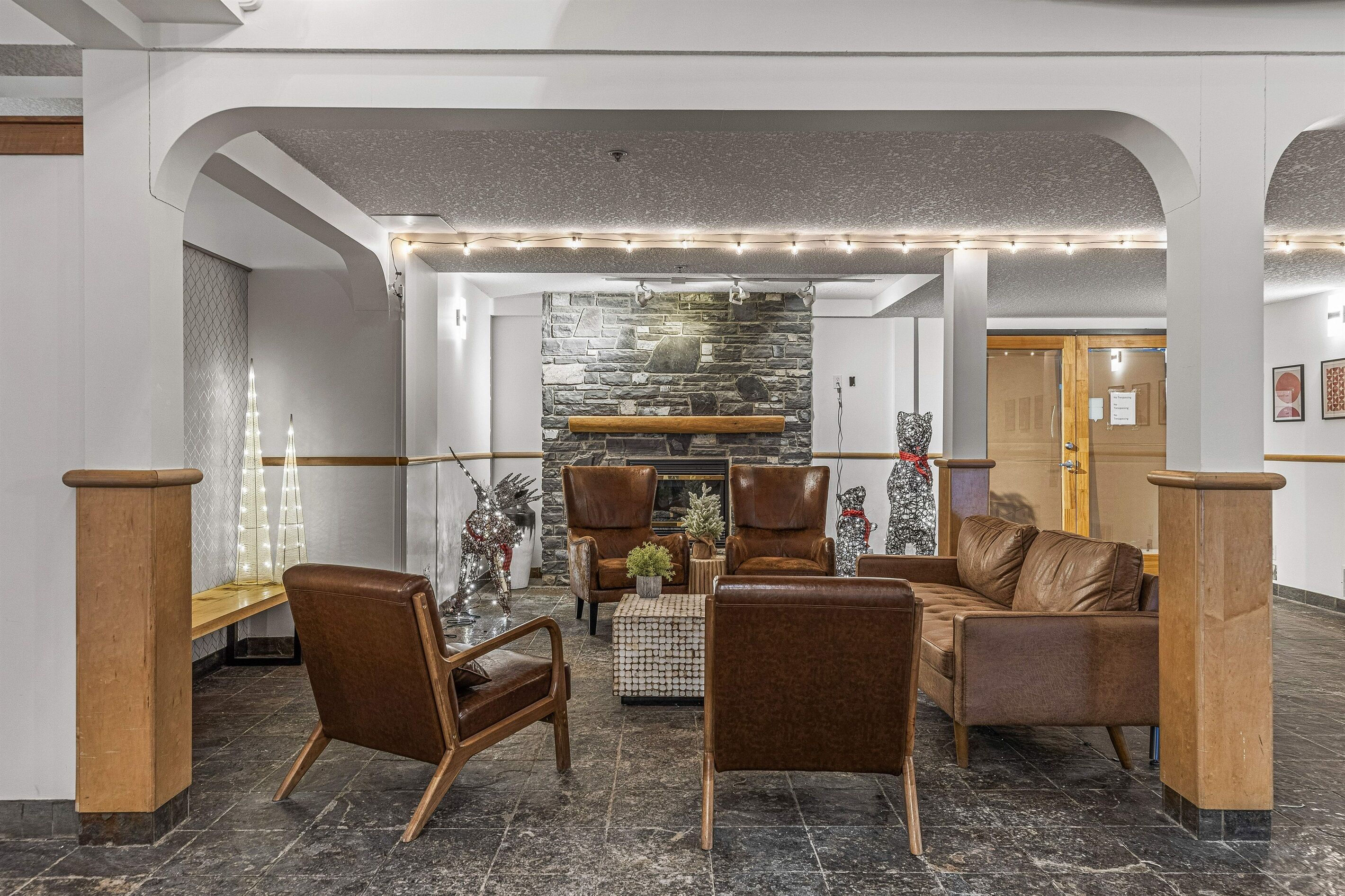 Un hall d’entrée avec un mur en pierre, des fauteuils en cuir, un banc en bois et une petite table agrémentée de plantes.