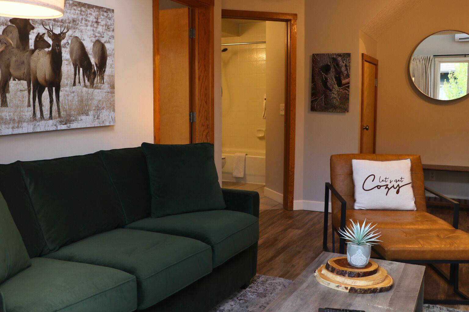 Ein Wohnzimmer mit einem grünen Sofa, einem braunen Ledersessel, einem Couchtisch mit Pflanze und einem Wandspiegel.