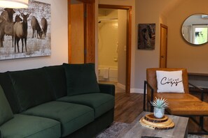 Een woonkamer met een groene bank, een bruine leren fauteuil, een salontafel met een plant en een spiegel aan de muur.