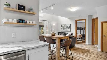 Una cucina moderna con mobili bianchi, un piano di lavoro in marmo e un tavolo da pranzo in legno con sedie. Sui pensili sopra il bancone ci sono tazze e un cartello di benvenuto.