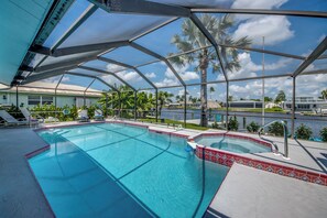 Une piscine dotée d’une structure en verre, bordée de palmiers et offrant une vue sur un port de plaisance.