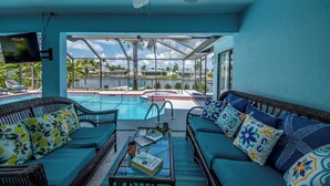 A poolside area with a sofa, a table with a book, and a television. - Wide Water Views, Hot Tub, Heated pool! 75 reviews.Villa 27 (Cape Coral)