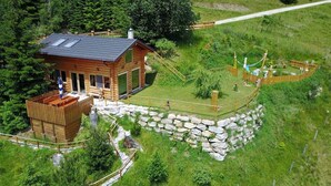 A wooden cabin with a stone wall and a small deck, surrounded by a fenced area and lush greenery. - Firefly and romantic hut, nature and wellness (Ratten)