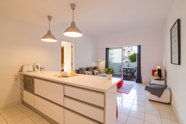 A modern kitchen with a central island, pendant lighting, and a view to a balcony.