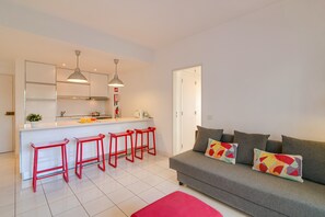 Una cocina moderna con armarios blancos, una isla central con taburetes y un sofá gris con cojines coloridos.