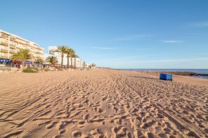 A sandy beach with footprints, palm trees, and a hotel in the background.