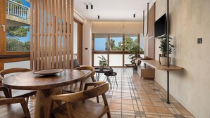 A modern dining area with a wooden table and chairs, large windows, and a view of the outdoors. - Xenios Dias Apartments (Chania)