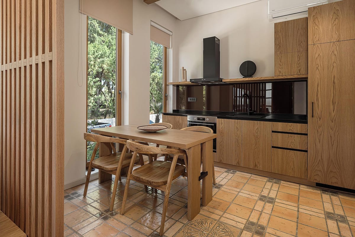 Eine moderne Küche mit Holzschränken, einer schwarzen Arbeitsplatte und einem Essbereich mit Holztisch und Stühlen.