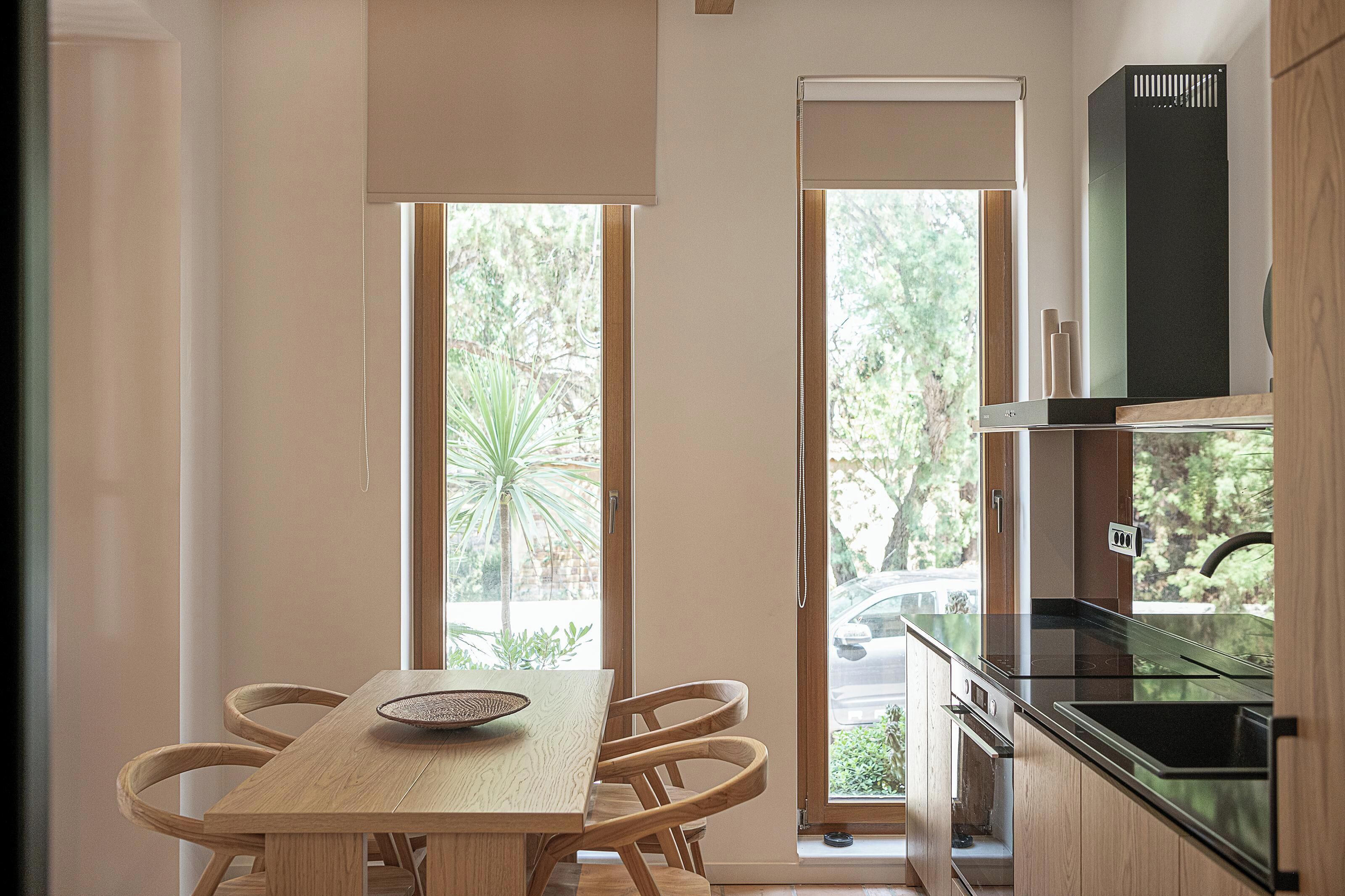 A kitchen with a wooden table, chairs, a stove, and a window with a view of trees and a car outside.