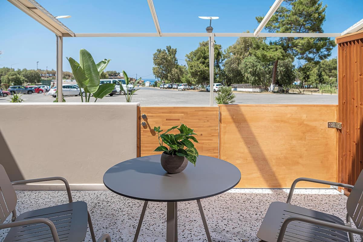 Ein Balkon mit rundem Tisch, zwei Stühlen, einem Blumentopf und Blick auf einen Parkplatz sowie Bäume.