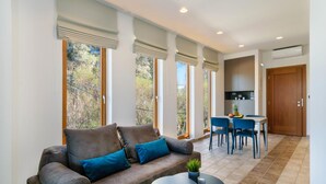 A modern living room with a sofa, a round coffee table, and a dining area with chairs and a table. - Xenios Dias Apartments (Chania)