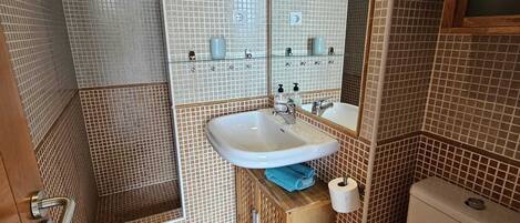A bathroom with a sink, mirror, toilet, and shower.