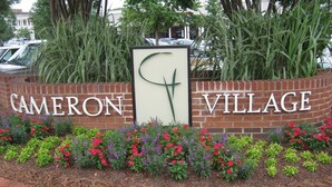 A sign for Cameron Village with a large 'C' and 'V' in the center, surrounded by a brick wall and colorful flower beds. - Comfortable and Quiet Condo near the Village and NC State (Raleigh)