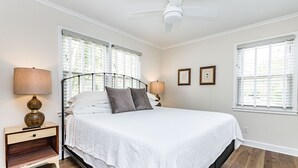 A bedroom with a bed, nightstand, lamp, ceiling fan, and two windows with blinds. - Comfortable and Quiet Condo near the Village and NC State (Raleigh)