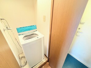 Eine kompakte, weiße Wasch-Trockner-Kombination in einem kleinen Waschraum mit Holztür und freiliegender Wasserleitung.