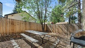 A backyard with a wooden fence, a picnic table, a barbecue grill, and a stone pathway. - Modern Times - Partial AC, Close to Lake & Village, Jet Tub, Fireplace, Barbecue (Big Bear Lake)