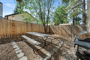 A backyard with a wooden fence, a picnic table, a barbecue grill, and a stone pathway. - Modern Times - Partial AC, Close to Lake & Village, Jet Tub, Fireplace, Barbecue (Big Bear Lake)