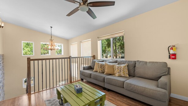 A spacious living room with a ceiling fan, a green coffee table, a grey sofa with patterned cushions, and a fire extinguisher mounted on the wall. - Modern Times - Partial AC, Close to Lake & Village, Jet Tub, Fireplace, Barbecue (Big Bear Lake)
