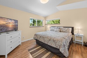 A bedroom with a bed, a dresser, a TV, and two windows.