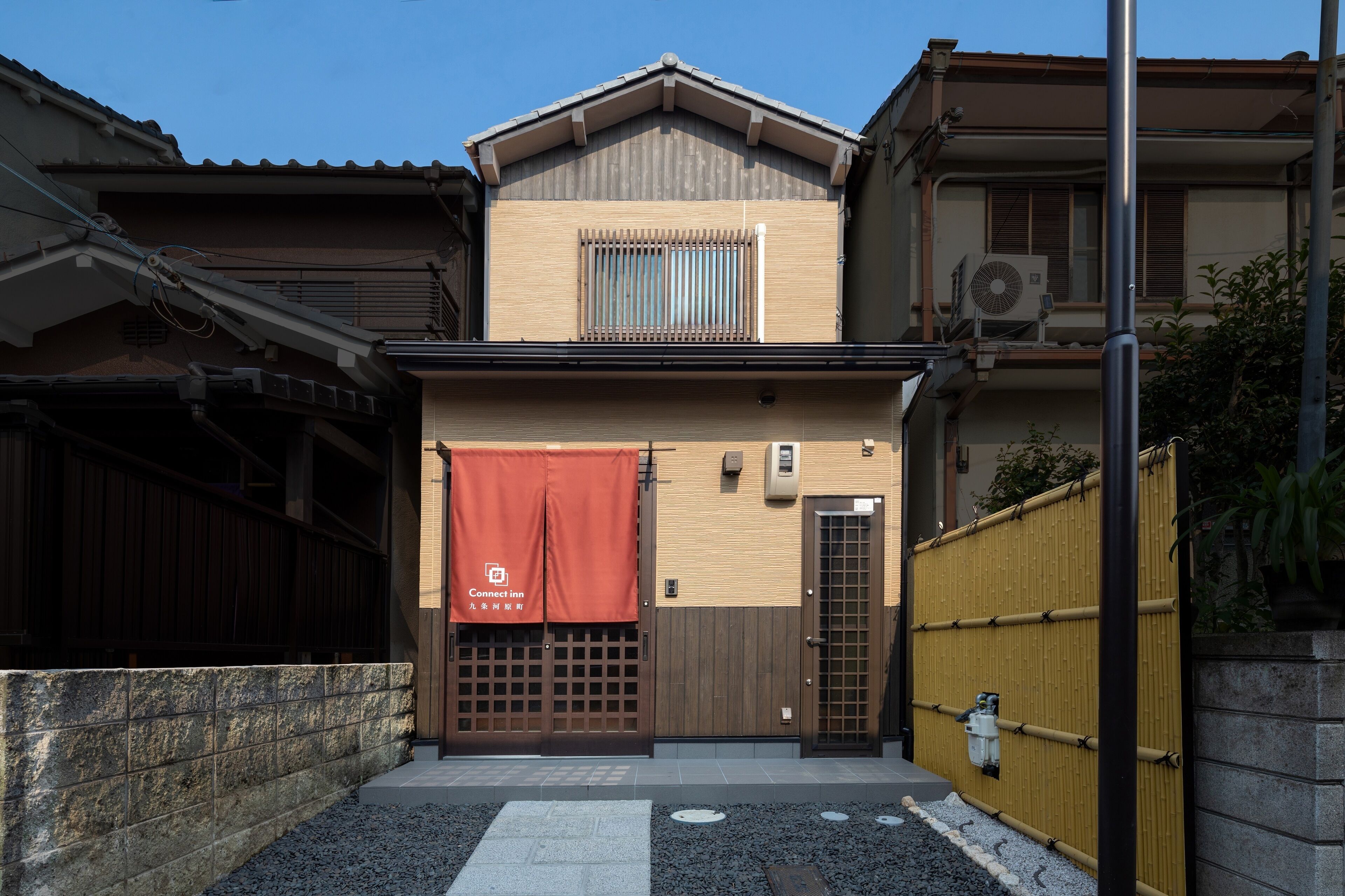 A two-story building with a wooden gate, a red banner, and a small garden area with stepping stones.