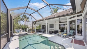 A pool area with a glass enclosure, outdoor seating, and a covered patio. - Waterfront Home on Key Lot | Pool & Sundeck (Marco Island)