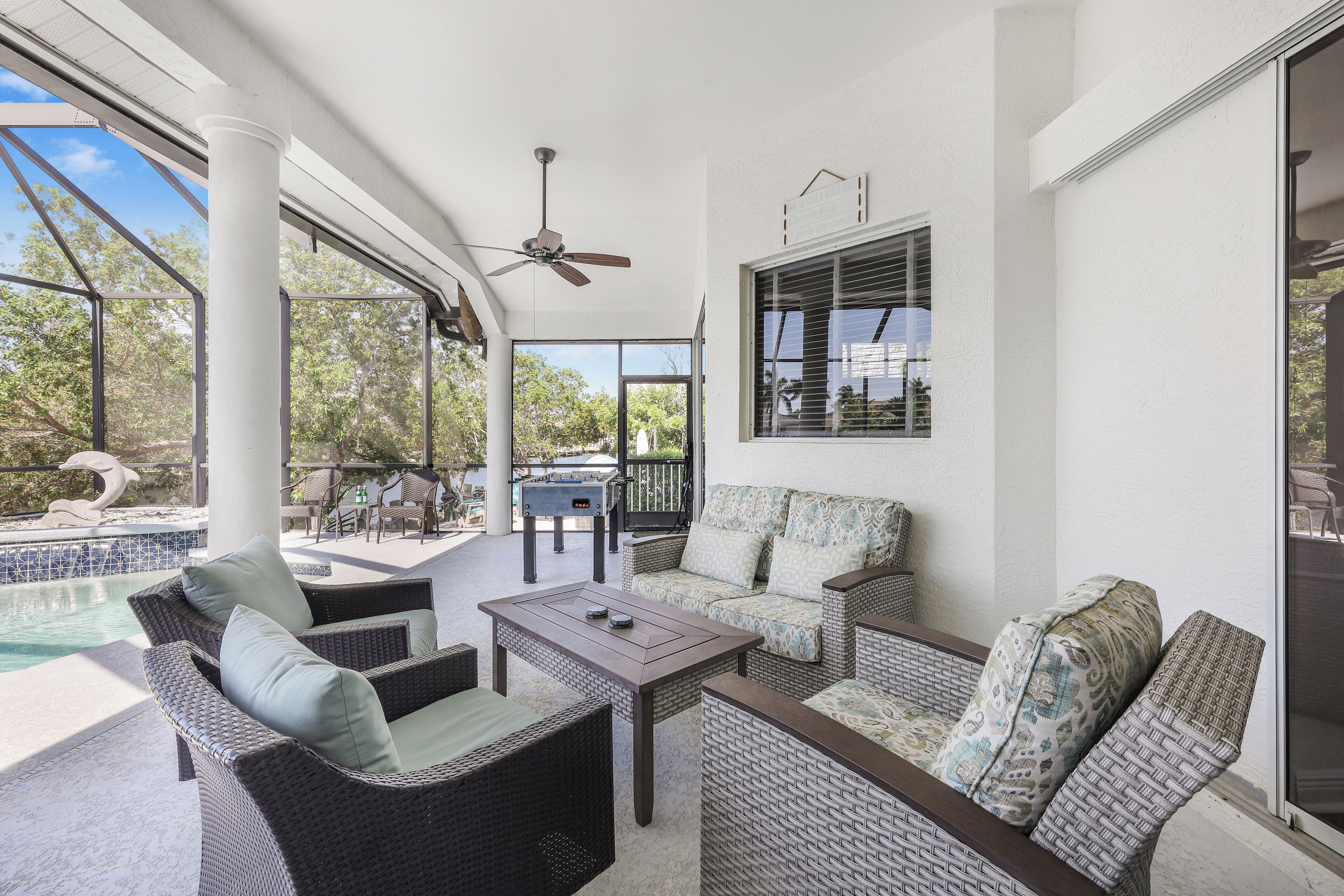 A covered patio area with wicker furniture, a ceiling fan, and a view of a swimming pool.