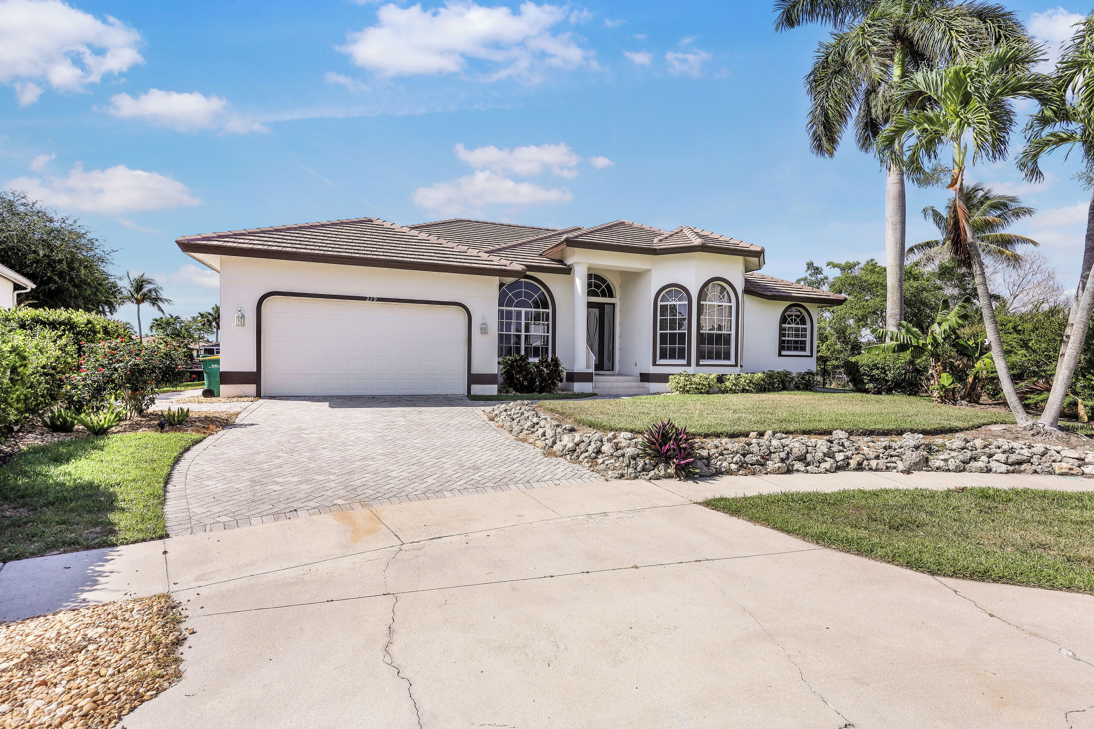 A single-story house with a garage, a driveway, and a well-maintained lawn with palm trees.