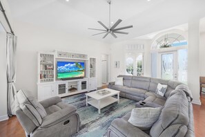 A spacious living room with a large grey sectional sofa, a white coffee table, and a flat-screen TV on a white entertainment unit. - Waterfront Home on Key Lot | Pool & Sundeck (Marco Island)