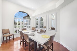 A dining room with a white table, six chairs, and large windows with arched tops. - Waterfront Home on Key Lot | Pool & Sundeck (Marco Island)