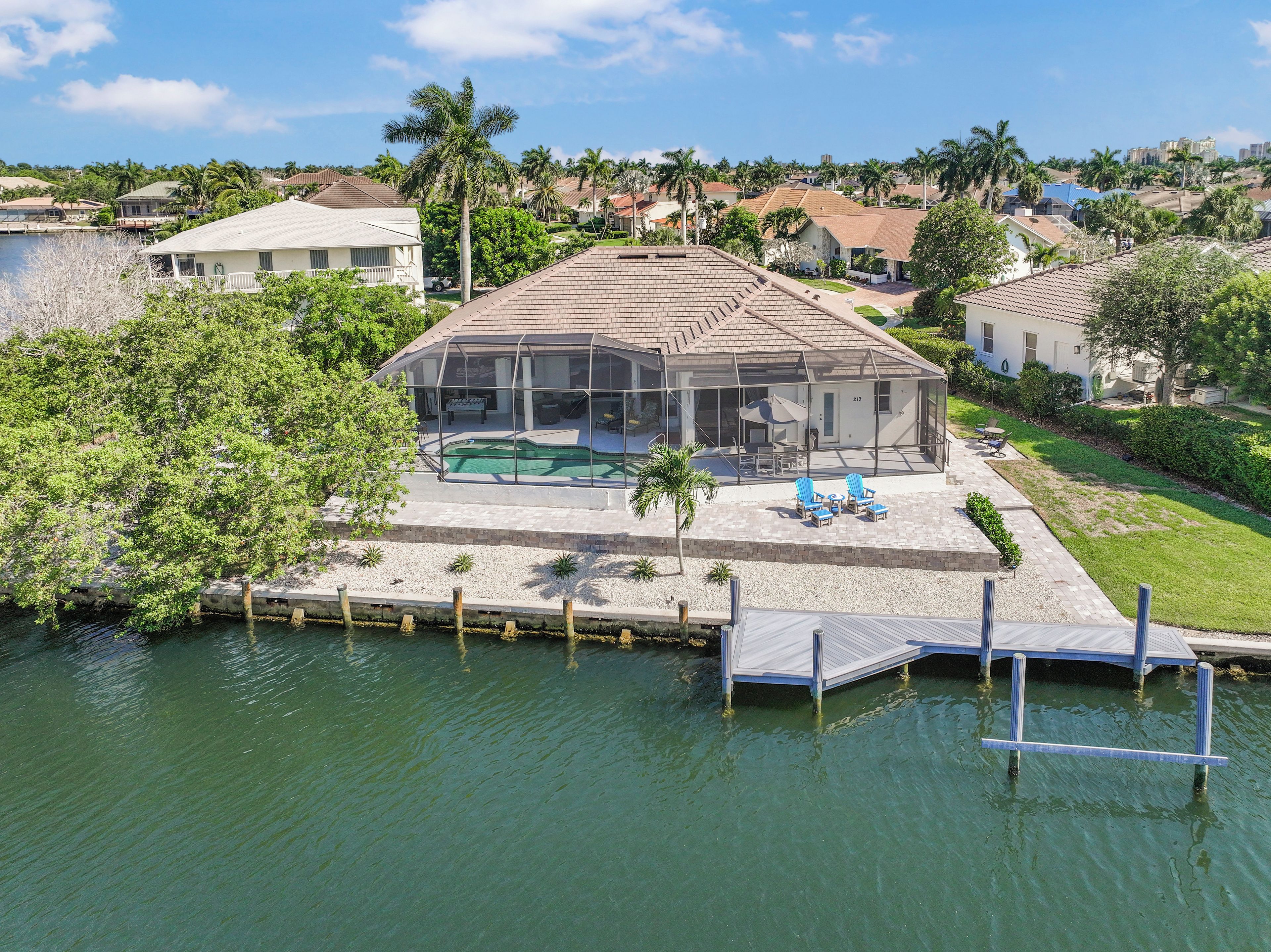 A house with a pool, surrounded by greenery and a dock extending into a body of water.