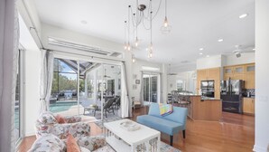 A spacious living area with a sofa, coffee table, and a blue couch. A kitchen with modern appliances is visible in the background. - Waterfront Home on Key Lot | Pool & Sundeck (Marco Island)