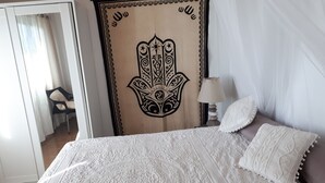 En säng med ett vitt överkast och kuddar, en sänglampa och en vägg med en dekorativ träpanel som föreställer en hand.